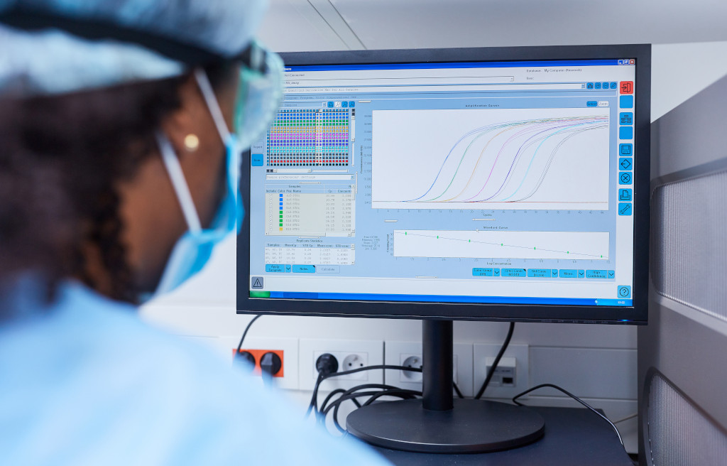 Photo of a black scientist with a cap, glasses and a protective mask looking at a
computer screen with various technical information with colors and colored lines.